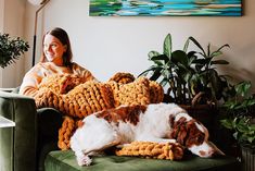 a woman is sitting on a couch with her dog and crocheted afghans