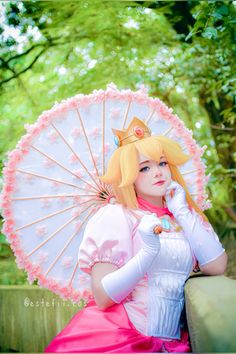 a woman in a pink dress is holding an umbrella and posing for the camera with her hand on her chin