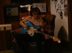 a man sitting in a chair with an electric guitar and headphones around his neck