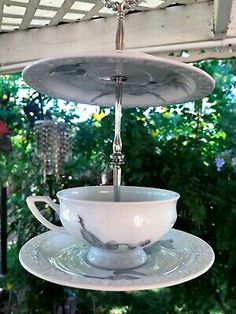 a tea cup and saucer hanging from a ceiling in front of a house with trees