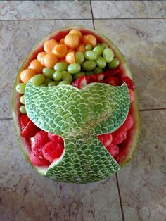 a watermelon bowl with grapes, melons and other fruits in it on a tile floor