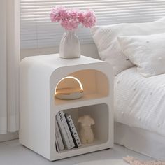 a white shelf with books and a pink flower in it