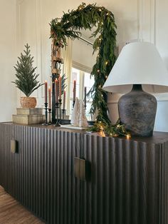 a christmas wreath on top of a dresser next to a lamp and other holiday decorations