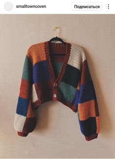 a multicolored cardigan sweater hanging on a white wall next to a hanger