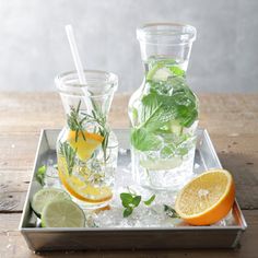 two glasses filled with water, lemons and mint on top of an ice tray