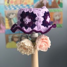 a crocheted hat on top of a wooden stick with flowers in the foreground