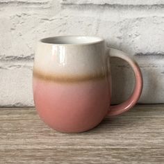 a pink and white coffee mug sitting on top of a wooden table next to a brick wall