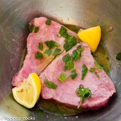 two pieces of meat in a metal bowl with lemon wedges