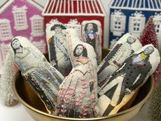 decorative fabric dolls are in a bowl next to small christmas trees and birdhouses on the table