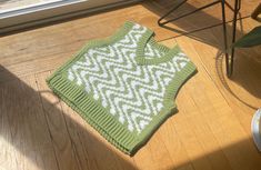 a green and white knitted blanket sitting on top of a wooden floor next to a window