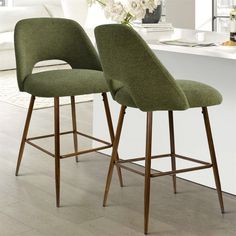 two green bar stools sitting in front of a white counter top with flowers on it