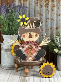 a wooden scarecrow sitting on top of a table with sunflowers in the background