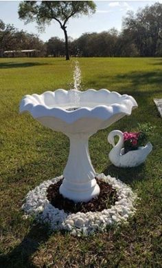 a white bird bath sitting on top of a grass covered field next to a flower pot