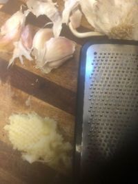 garlic being grated on top of a cutting board with a grater next to it