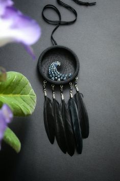 a necklace with beads and feathers hanging from it's side on a table next to purple flowers