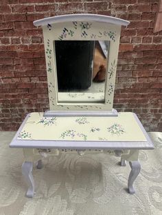 a small white vanity with a mirror on it's side and flowers painted on the top