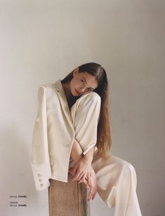 a woman sitting on top of a wooden box with her legs crossed and wearing a white suit