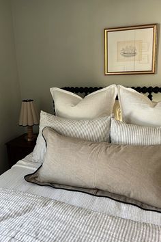 a bed with white and gray pillows in a bedroom next to a painting on the wall