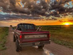 a red truck parked on the side of a dirt road next to a lush green field