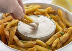 a person dipping sauce on french fries in a bowl