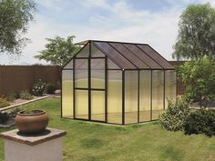 a small glass house sitting in the middle of a green yard next to a large potted plant