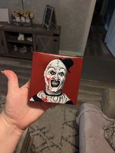 a person holding up a small card with a painting of a clown on it's face