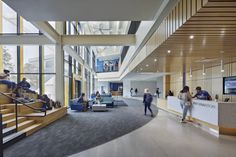 people are sitting and walking around in the lobby at an office building with large windows