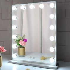 a vase with flowers in it sitting next to a large mirror that has lights on