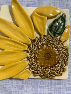 a yellow sunflower with green leaves on a white plate