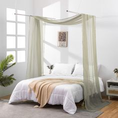 a bed with a canopy and pillows in a white room next to a potted plant