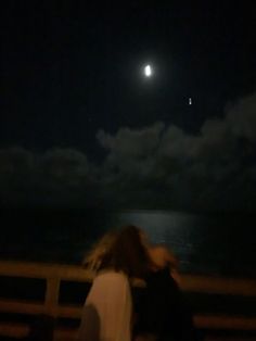 two people standing on a pier looking at the moon