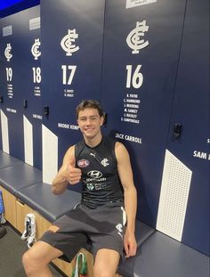 a man sitting on top of a bench in front of lockers giving the thumbs up