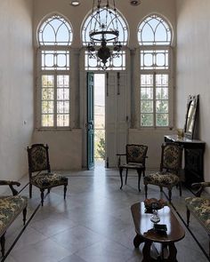 a living room filled with lots of furniture next to two large windows and a chandelier hanging from the ceiling