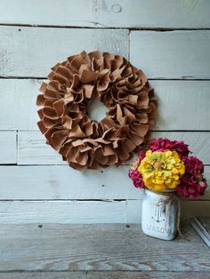 a mason jar filled with flowers next to a wreath on a wooden wall behind it