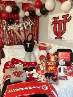 a woman sitting on top of a bed surrounded by red and white balloons, streamers and decorations