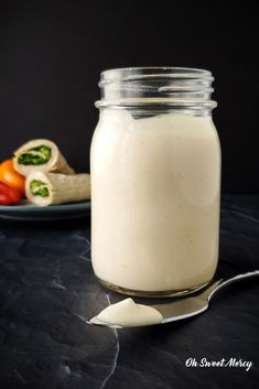 a glass jar filled with white liquid next to a plate of food on a table