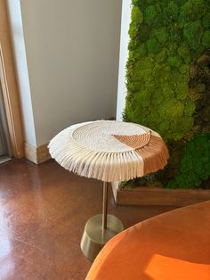 a round table with fringes on it in front of a moss wall and orange couch