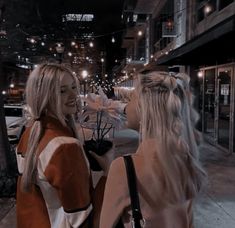 two women standing on the side walk talking to each other in the city at night