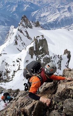 a man climbing up the side of a snow covered mountain with mountains in the background