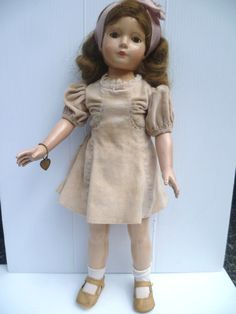 a doll with brown hair wearing a tan dress and beige shoes is standing in front of a white wall