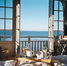 two cups of coffee sit on a tray in front of an open window overlooking the ocean