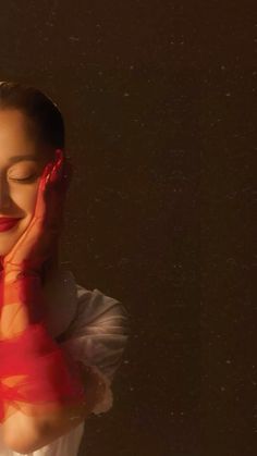 a woman in white shirt holding her hands to her face with red ribbon around her neck