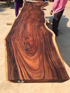 a large wooden slab is being worked on by two men in pink shirts and purple pants