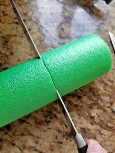 a person cutting green paper with scissors on a counter next to a roll of toilet paper