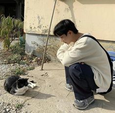 a man kneeling down next to a black and white cat laying on the ground in front of a building