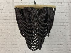 a chandelier made out of black beads hangs from a brick wall in front of a white brick wall