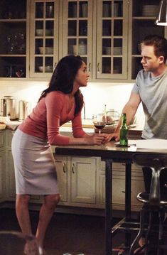 a man standing next to a woman at a kitchen counter with a wine glass in her hand