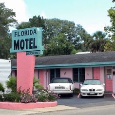 two cars parked in front of a motel with pink walls and palm trees behind it