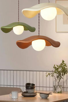 three different colored lights hanging from the ceiling above a dining room table with plates and cups on it