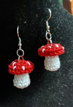 red and white mushroom earrings on a black surface